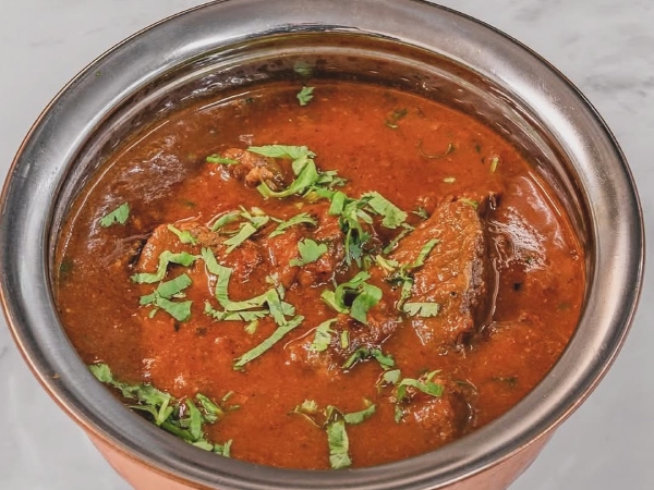 A bowl of Mallroad House Rogan Josh, a reddish-brown Indian lamb curry with a thick and rich sauce.